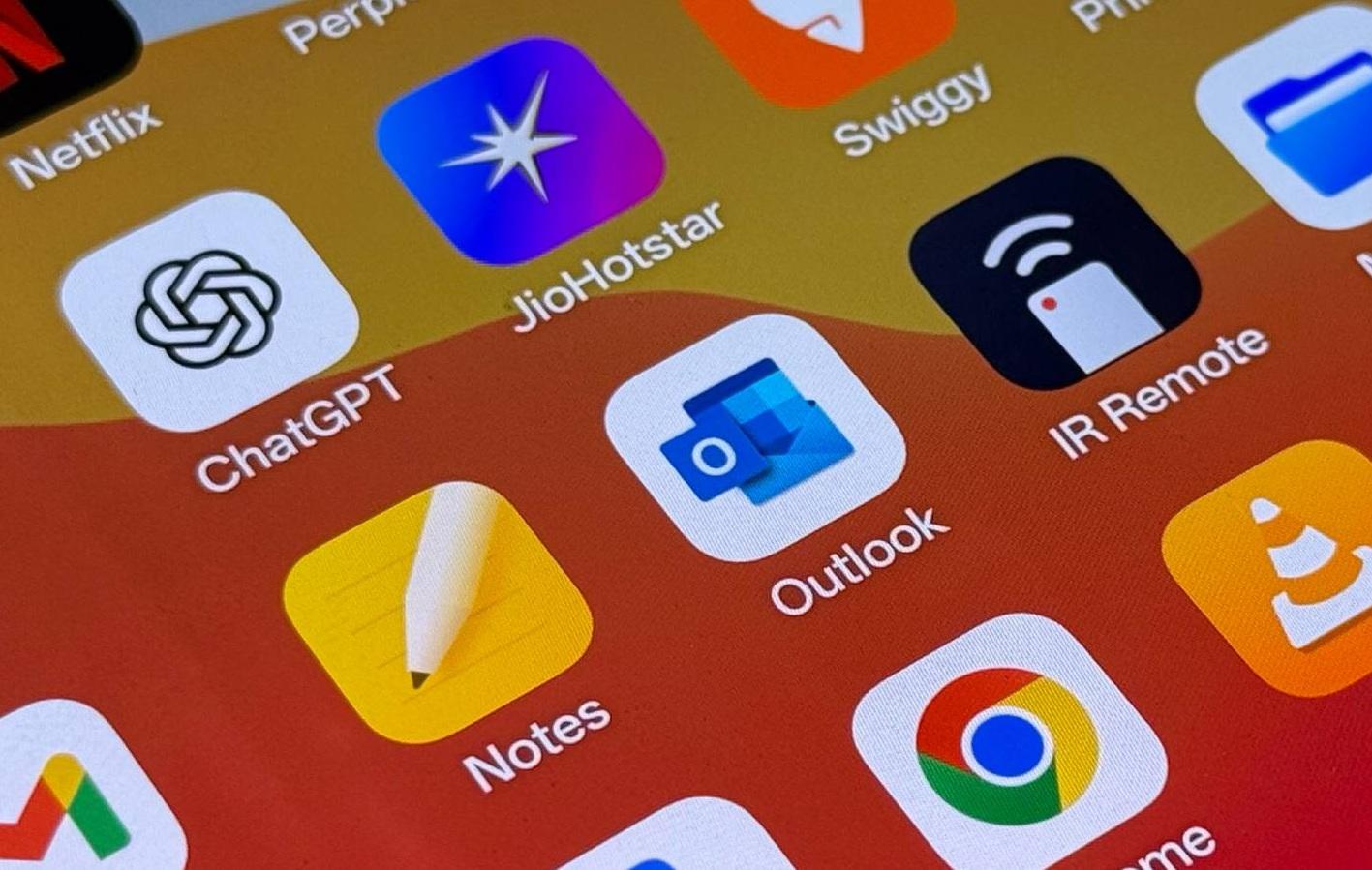 Экран смартфона с иконками приложений: Netflix, ChatGPT, JioHotstar, Outlook, Notes, Chrome и другие. Градиентный фон от жёлтого к красному.
